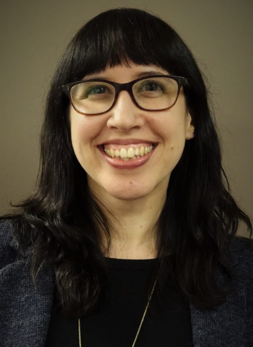 Prof Ruth Kramer is a white woman with black hair, wearing square glasses and a black suit