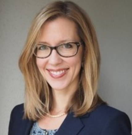 Prof. Alex Johnston is a white woman with blonde hair and blue eyes. She is wearing dark-framed glasses, a blue shirt, blue blazer and pearl necklace. 