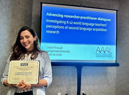 Caitlyn posing with her award in front of a monitor displaying her presentation. 