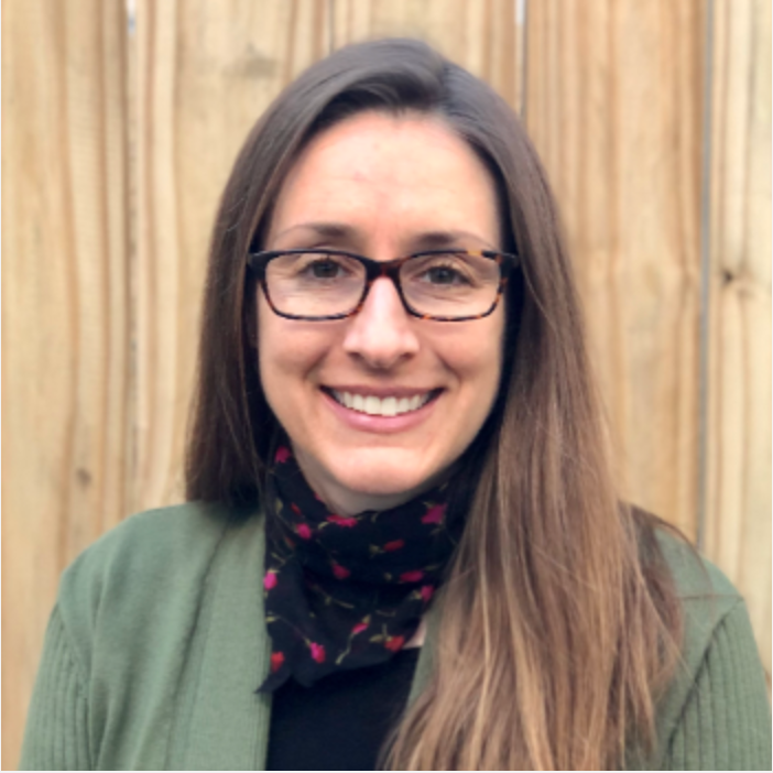 This is a portrait of Prof. Cynthia Gordon. She is a white woman with straight, light brown hair, wearing square glasses,  a black short, sage green jacket, and a floral black and red scarf. 