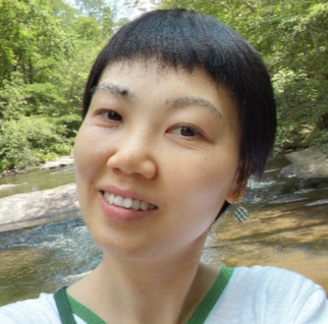 Dr. Laura Tan is an Asian woman with black pixie cute hair and brown eyes. She is wearing a white t-shirt with a green lining. 