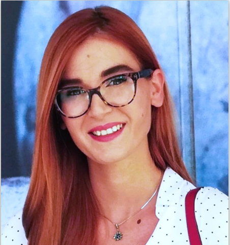 Headshot of Maša Bešlin with red hair and glasses, smiling against a blue backdrop